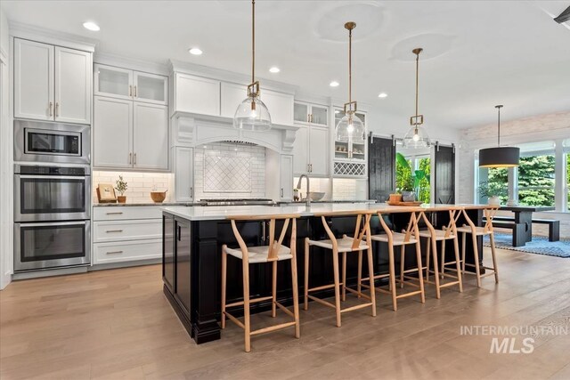 1552 W Windbreaker Ln, Eagle, ID 83616 - kitchen featuring appliances with stainless steel finishes, a large island with sink, light wood-style flooring, decorative backsplash, and recessed lighting