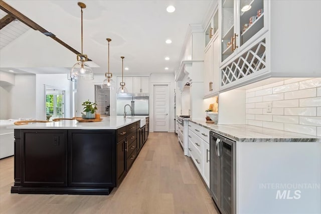 1552 W Windbreaker Ln, Eagle, ID 83616 - kitchen featuring beverage cooler, white cabinets, light wood-type flooring, tasteful backsplash, and a large island with sink