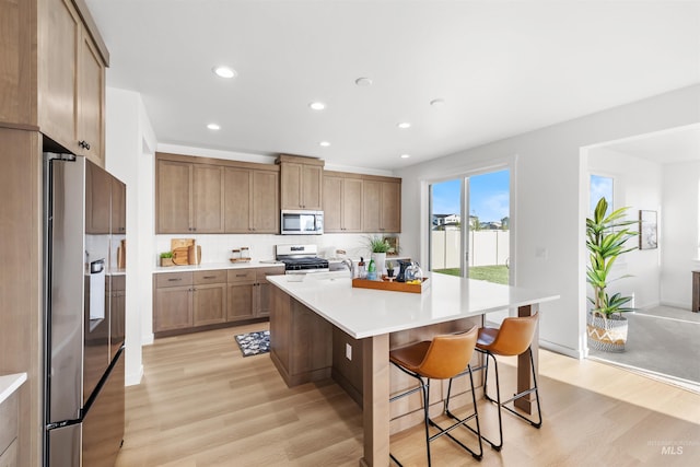 kitchen with appliances with stainless steel finishes, light wood-style flooring, a breakfast bar, light countertops, and recessed lighting
