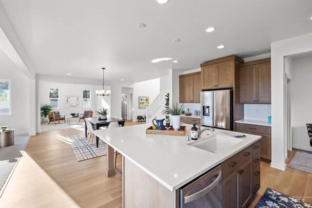 kitchen featuring appliances with stainless steel finishes, a sink, light wood-style flooring, tasteful backsplash, and light countertops