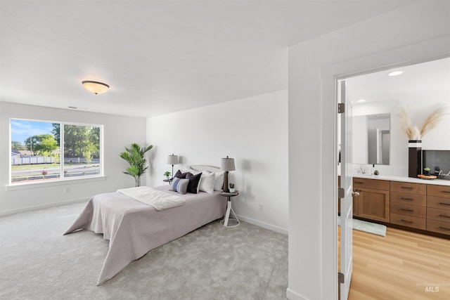 bedroom featuring baseboards, light carpet, ensuite bath, and a sink