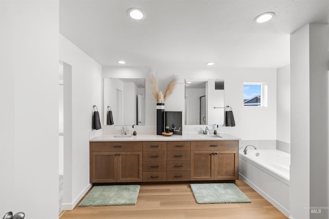 full bathroom with wood finished floors, a bath, double vanity, and recessed lighting