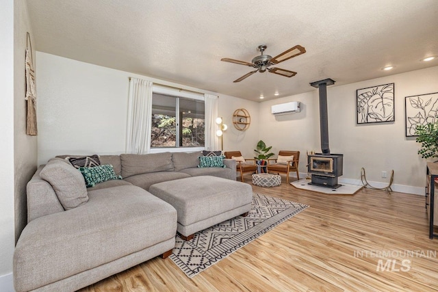 living room with a wood stove, an AC wall unit, a ceiling fan, and wood finished floors