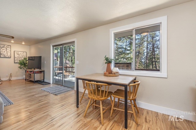 dining area with light wood-style floors, baseboards, and a textured ceiling