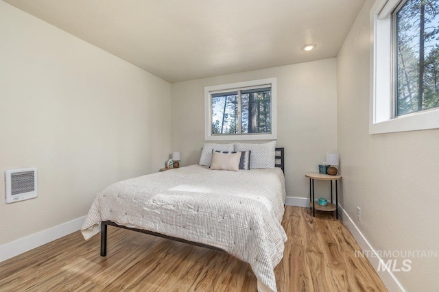 bedroom featuring baseboards, heating unit, and wood finished floors