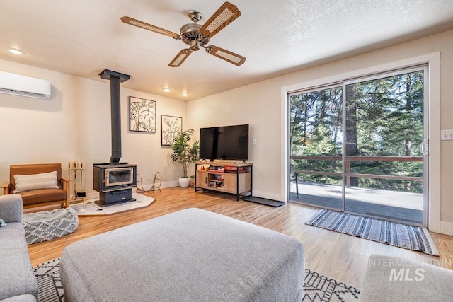 living area featuring a wall mounted air conditioner, a wood stove, a wealth of natural light, and ceiling fan
