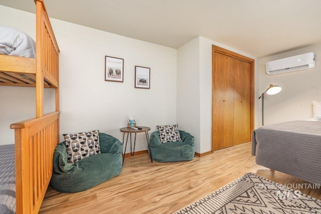 bedroom featuring a wall mounted air conditioner, light wood-style flooring, a closet, and baseboards