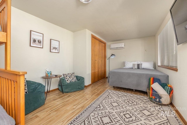bedroom with a closet, light wood-style flooring, an AC wall unit, and baseboards