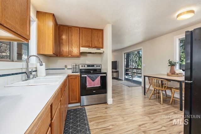 kitchen featuring light wood-type flooring, freestanding refrigerator, under cabinet range hood, electric stove, and a sink