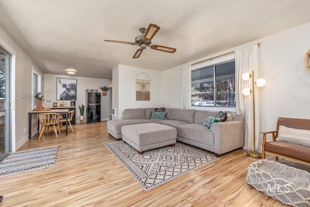 living room featuring a textured ceiling, wood finished floors, baseboards, and a ceiling fan