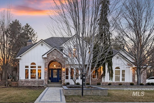 view of front of house featuring brick siding, a yard, roof with shingles, board and batten siding, and a chimney