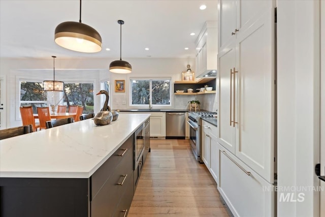 kitchen with a center island, white cabinetry, appliances with stainless steel finishes, light wood-type flooring, and decorative backsplash