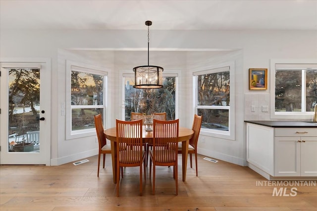 dining area with light wood-style flooring, an inviting chandelier, visible vents, and baseboards