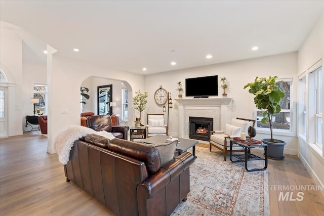 living room with arched walkways, recessed lighting, light wood-style floors, a lit fireplace, and baseboards