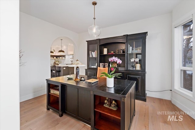 bar featuring arched walkways, baseboards, decorative light fixtures, and light wood-style floors