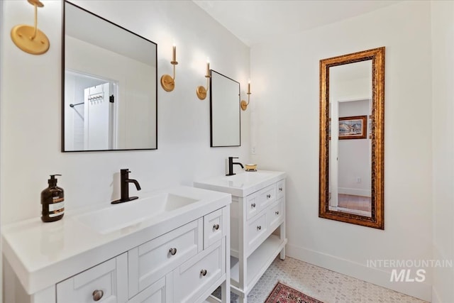 bathroom with baseboards, two vanities, a sink, and speckled floor