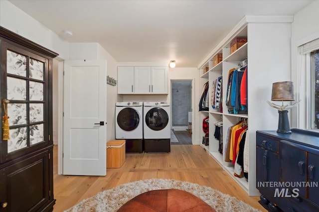 washroom with light wood-type flooring, washing machine and dryer, and cabinet space