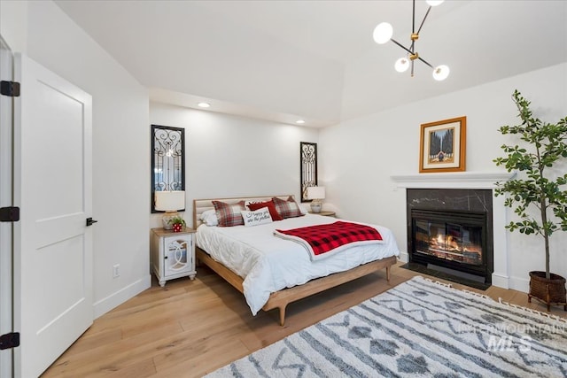 bedroom featuring a notable chandelier, recessed lighting, wood finished floors, a high end fireplace, and baseboards