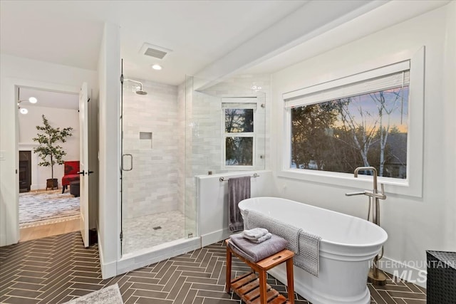 full bath featuring a stall shower, a soaking tub, visible vents, and baseboards