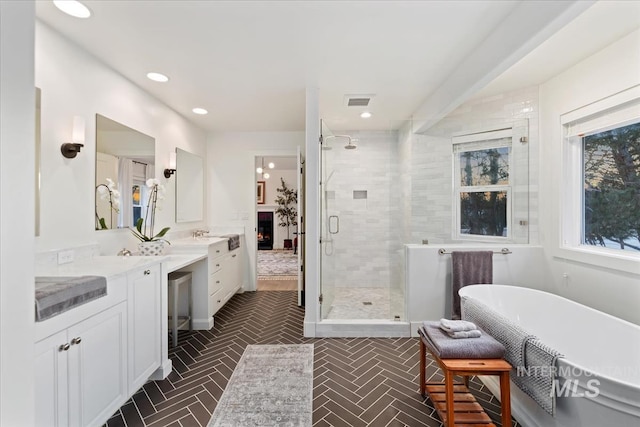 full bathroom with recessed lighting, a soaking tub, a stall shower, vanity, and a lit fireplace