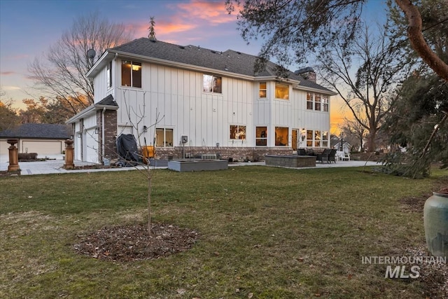 rear view of house featuring a chimney, an attached garage, a yard, a patio area, and board and batten siding