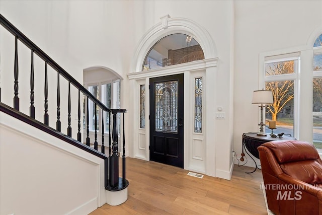 foyer entrance featuring a high ceiling, visible vents, baseboards, light wood-style floors, and stairway