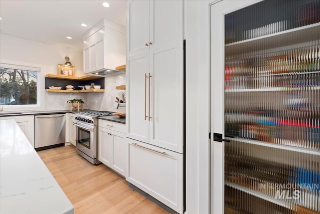 kitchen with light wood finished floors, open shelves, appliances with stainless steel finishes, white cabinetry, and premium range hood