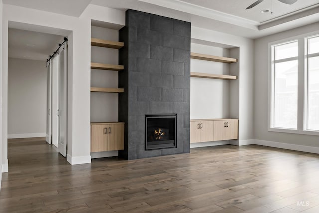 unfurnished living room featuring wood finished floors, a tile fireplace, a barn door, and built in shelves