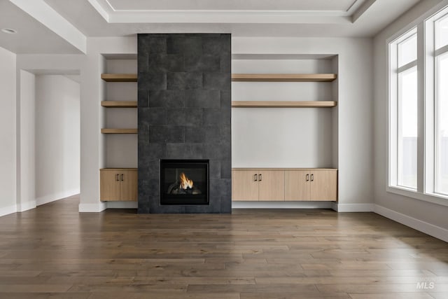 unfurnished living room featuring built in shelves, baseboards, a tiled fireplace, and wood finished floors