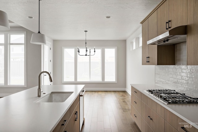 kitchen with light countertops, stainless steel appliances, a sink, decorative light fixtures, and under cabinet range hood