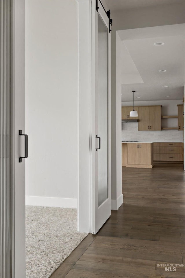 hallway with baseboards, dark wood-style flooring, and a barn door