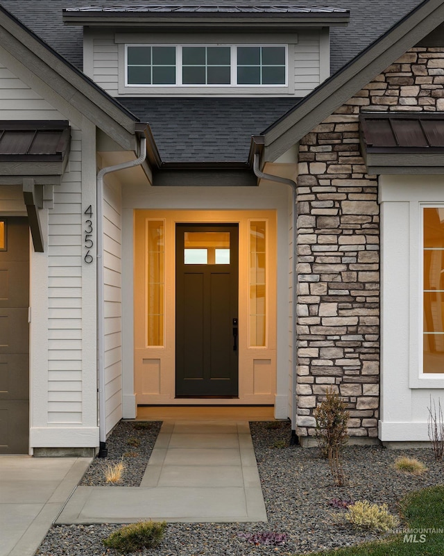 property entrance featuring roof with shingles, an attached garage, and stone siding