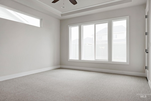 carpeted empty room with baseboards, ceiling fan, and a raised ceiling