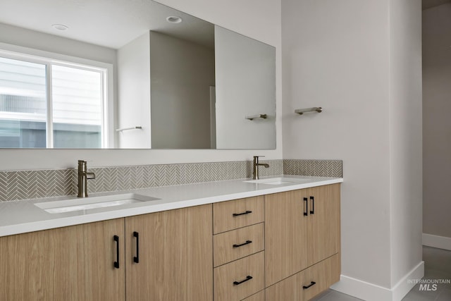 bathroom featuring a sink, baseboards, double vanity, and decorative backsplash