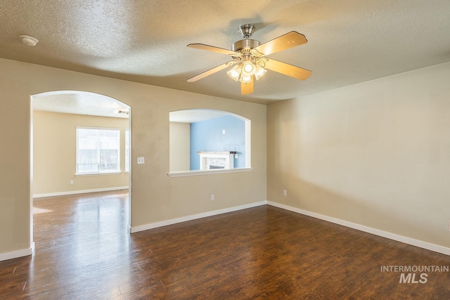 unfurnished room featuring a ceiling fan, dark wood-style flooring, a textured ceiling, and baseboards