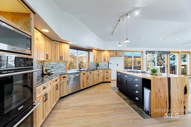 kitchen featuring a center island with sink, vaulted ceiling, light brown cabinetry, decorative light fixtures, and stainless steel appliances