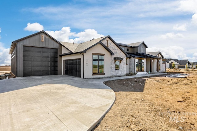 modern farmhouse with board and batten siding, concrete driveway, stone siding, and a garage