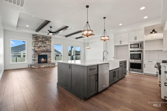 kitchen with white cabinets, appliances with stainless steel finishes, decorative light fixtures, beamed ceiling, and an island with sink