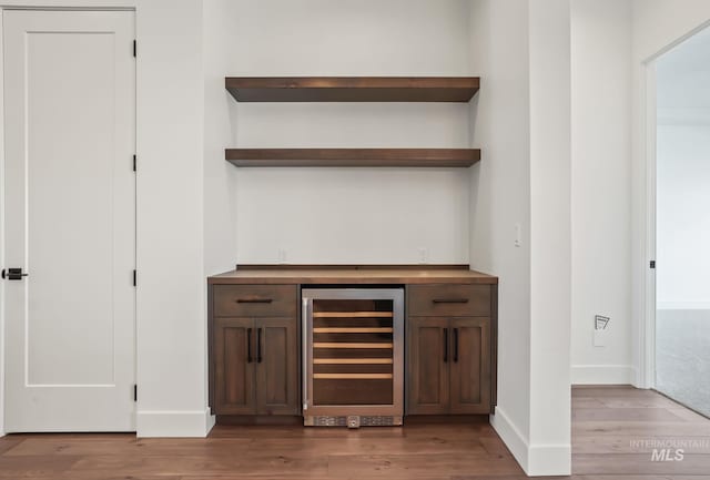 bar with light hardwood / wood-style floors, beverage cooler, and dark brown cabinetry