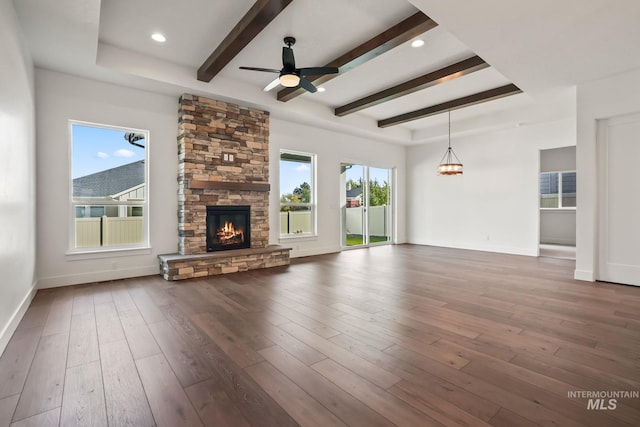 unfurnished living room featuring ceiling fan, a raised ceiling, dark hardwood / wood-style floors, and a stone fireplace