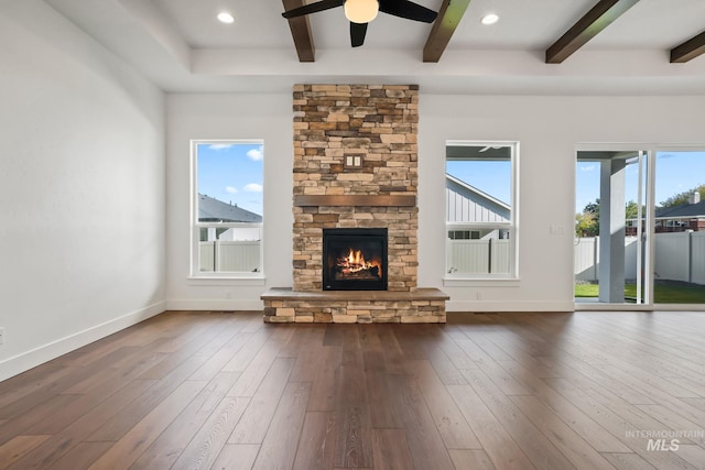 unfurnished living room with ceiling fan, dark wood-type flooring, beamed ceiling, and a stone fireplace