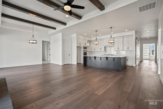 unfurnished living room with ceiling fan with notable chandelier, dark hardwood / wood-style flooring, beamed ceiling, sink, and a barn door