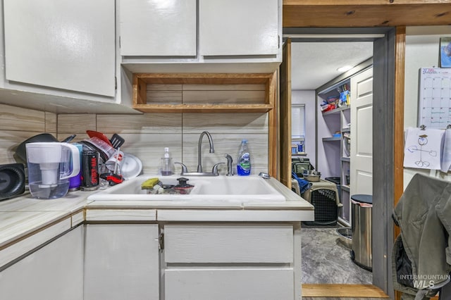 kitchen with decorative backsplash, white cabinetry, sink, and a textured ceiling