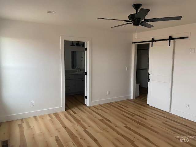 unfurnished bedroom featuring a spacious closet, connected bathroom, light hardwood / wood-style floors, and a barn door