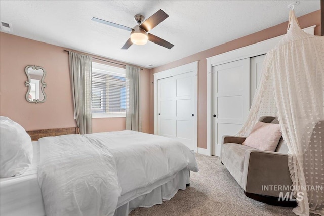 carpeted bedroom featuring a ceiling fan, visible vents, baseboards, multiple closets, and a textured ceiling