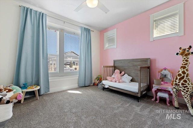 carpeted bedroom with a crib and ceiling fan