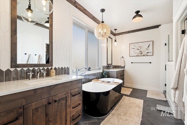 bathroom with backsplash, baseboards, two vanities, a soaking tub, and a sink