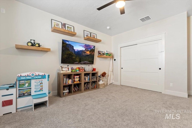 rec room with visible vents, a textured ceiling, carpet flooring, baseboards, and ceiling fan