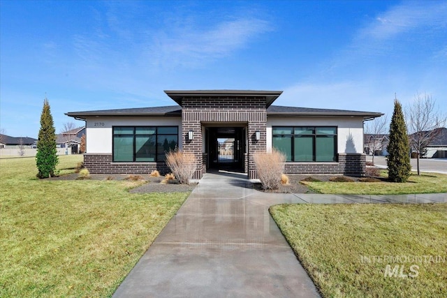 view of front of house featuring stucco siding, driveway, brick siding, and a front lawn