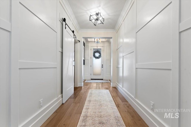 doorway with a barn door, a decorative wall, light wood-style floors, and ornamental molding